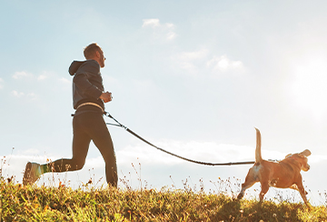 Jogger running through the countryside on a clear day with a dog on a lead